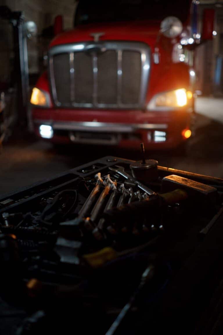 Dimly lit garage scene featuring tools and a red truck, suggesting automotive repair.