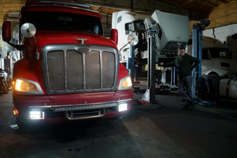 Red truck in a garage with mechanic and elevated vehicles undergoing maintenance.