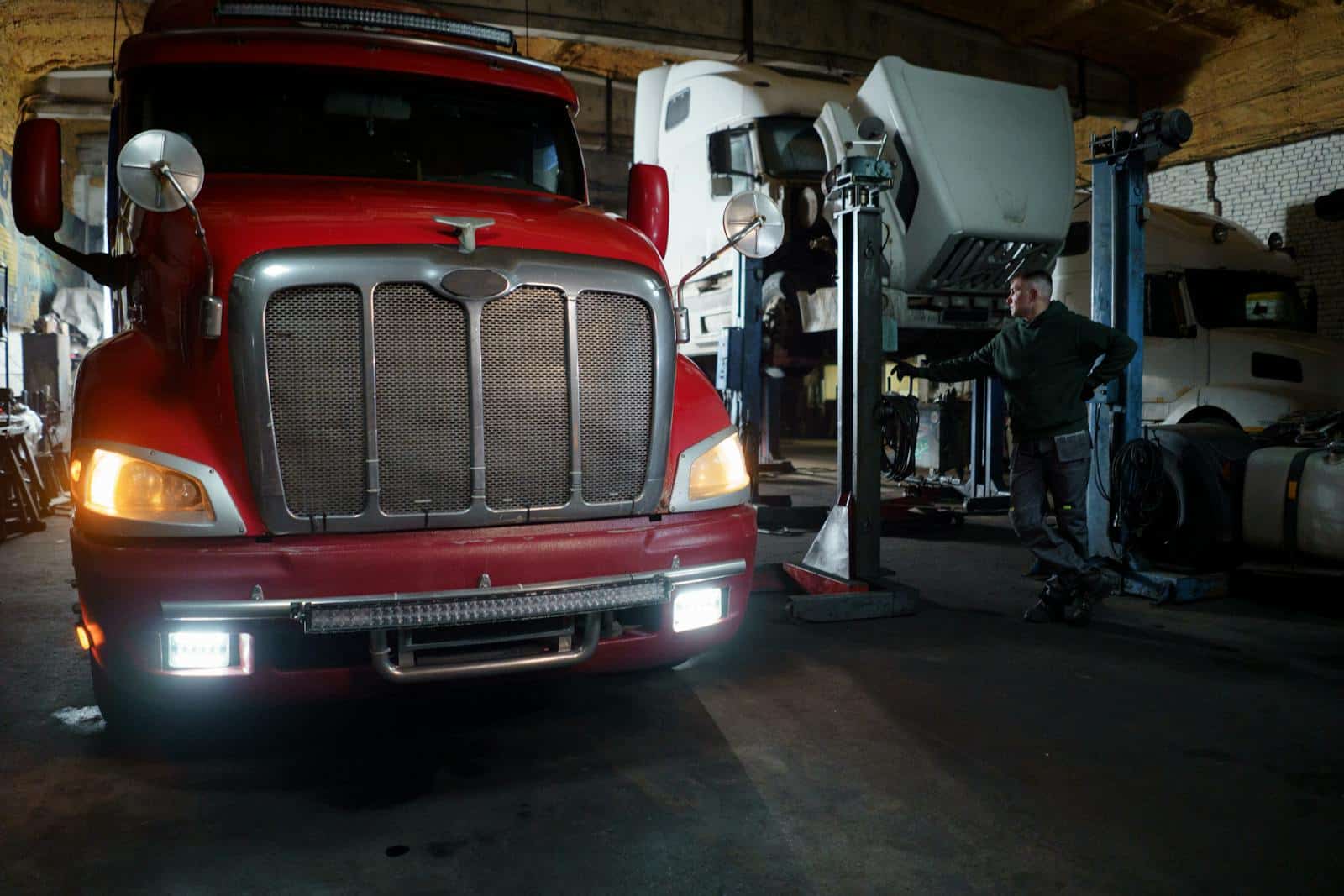 Red truck in a garage with mechanic and elevated vehicles undergoing maintenance.